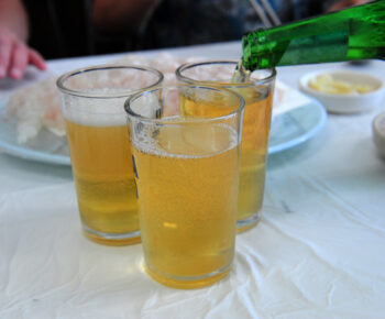 Three glasses of beer on a table, one of which is being filled by a green bottle