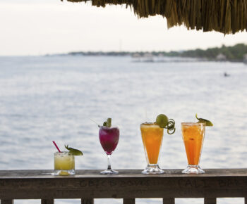 Four cocktails in a row in front of the ocean in Belize