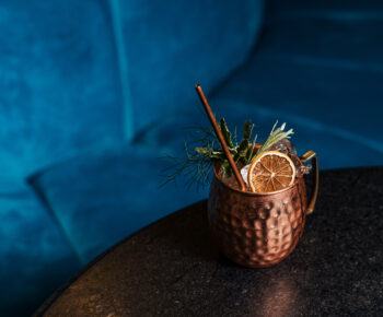 Copper mug on top of a table in front of a blue velvet sofa