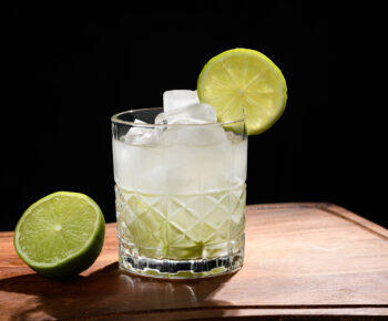 Cocktail glass on top of a table filled with limes and a clear liquid