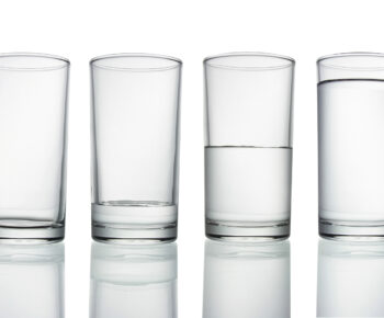 Four tall glasses filled with different levels of water on a white background