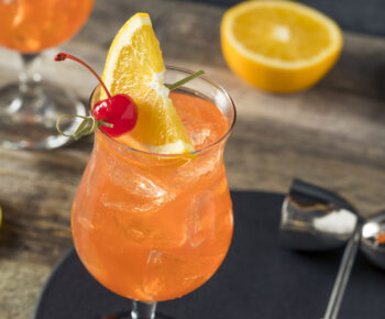 Orange cocktail with a slice of lemon and a cherry on top