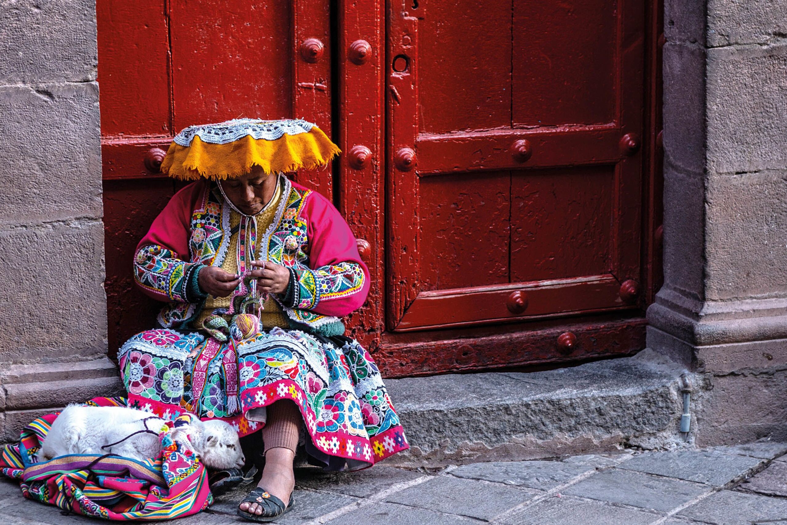 Lady sat on a step knitting, with a lamb by her feet
