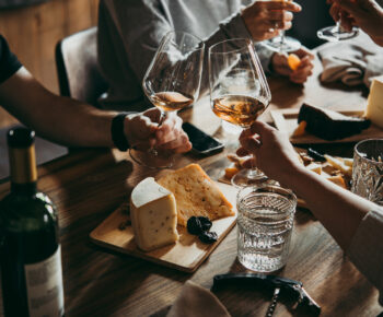 People clinking glasses of wine together over a cheese board