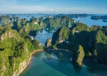 Aerial shot of Ha Long Bay during the daytime showing the towering limestone islands covered in green foliage and the surrounding waters