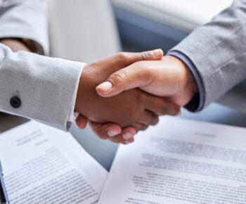 Close-up of two people shaking hands over a contract