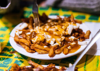 Plate of Montreal poutine with fries gravy and cheese curds on a white plate at a diner