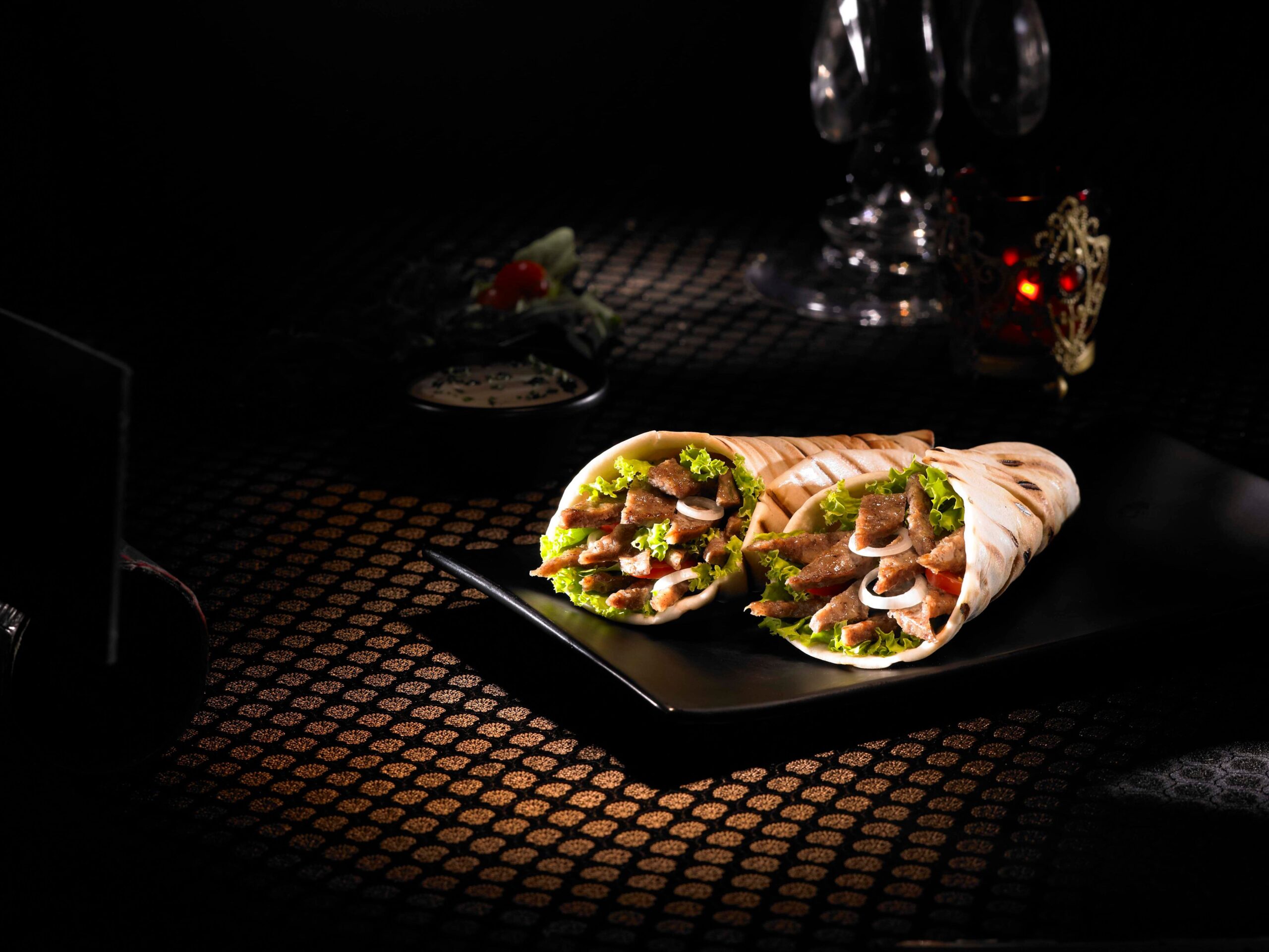 A pair of meat wraps on a black plate on the table