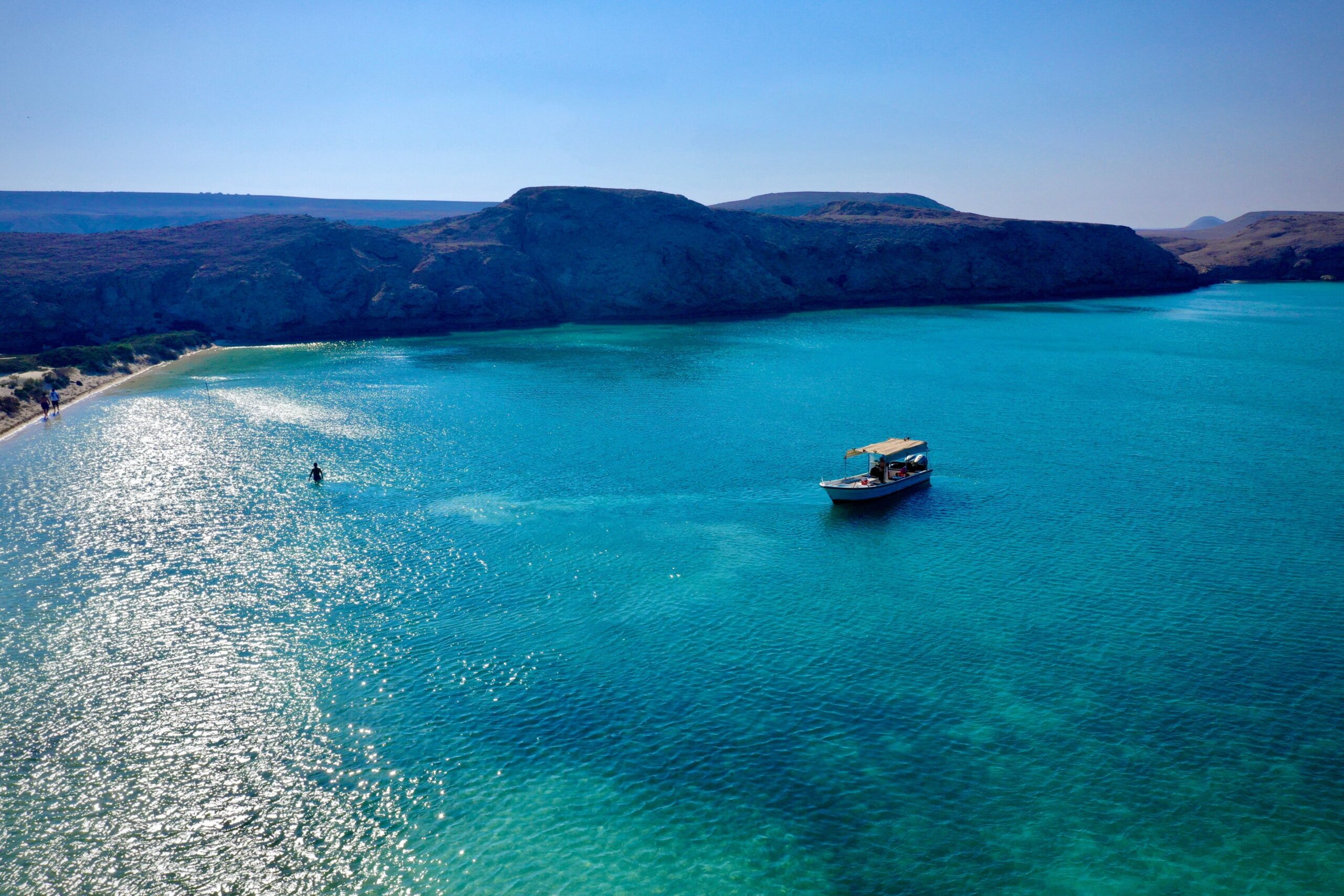 A boat in the blue seawater surrounding by rocky cliffs