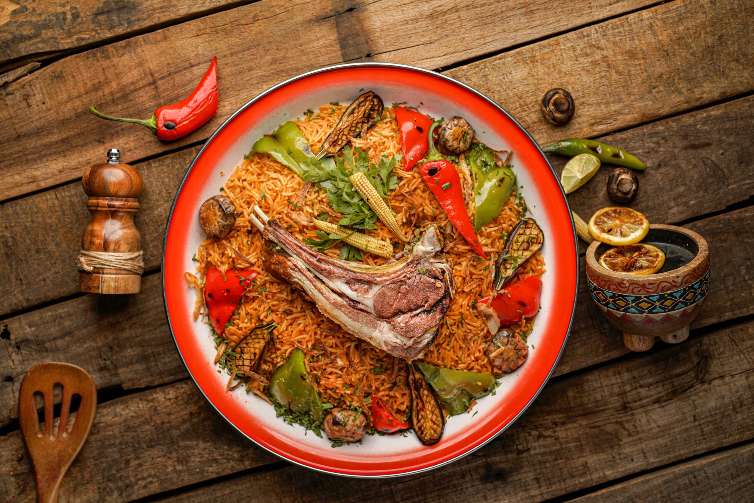 Lamb over a plate full of rice with vegetables on a wooden table