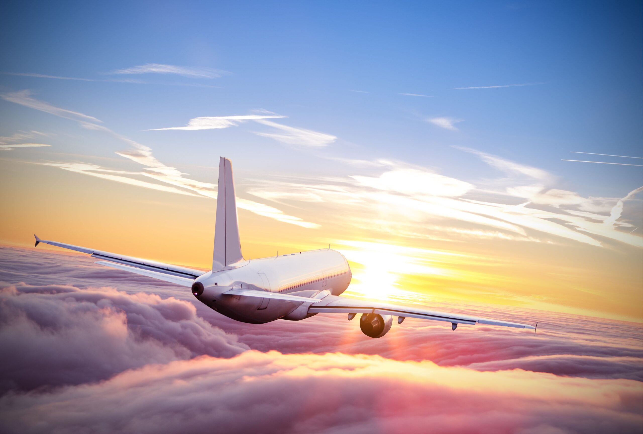 A plane flying towards the sunset above the clouds